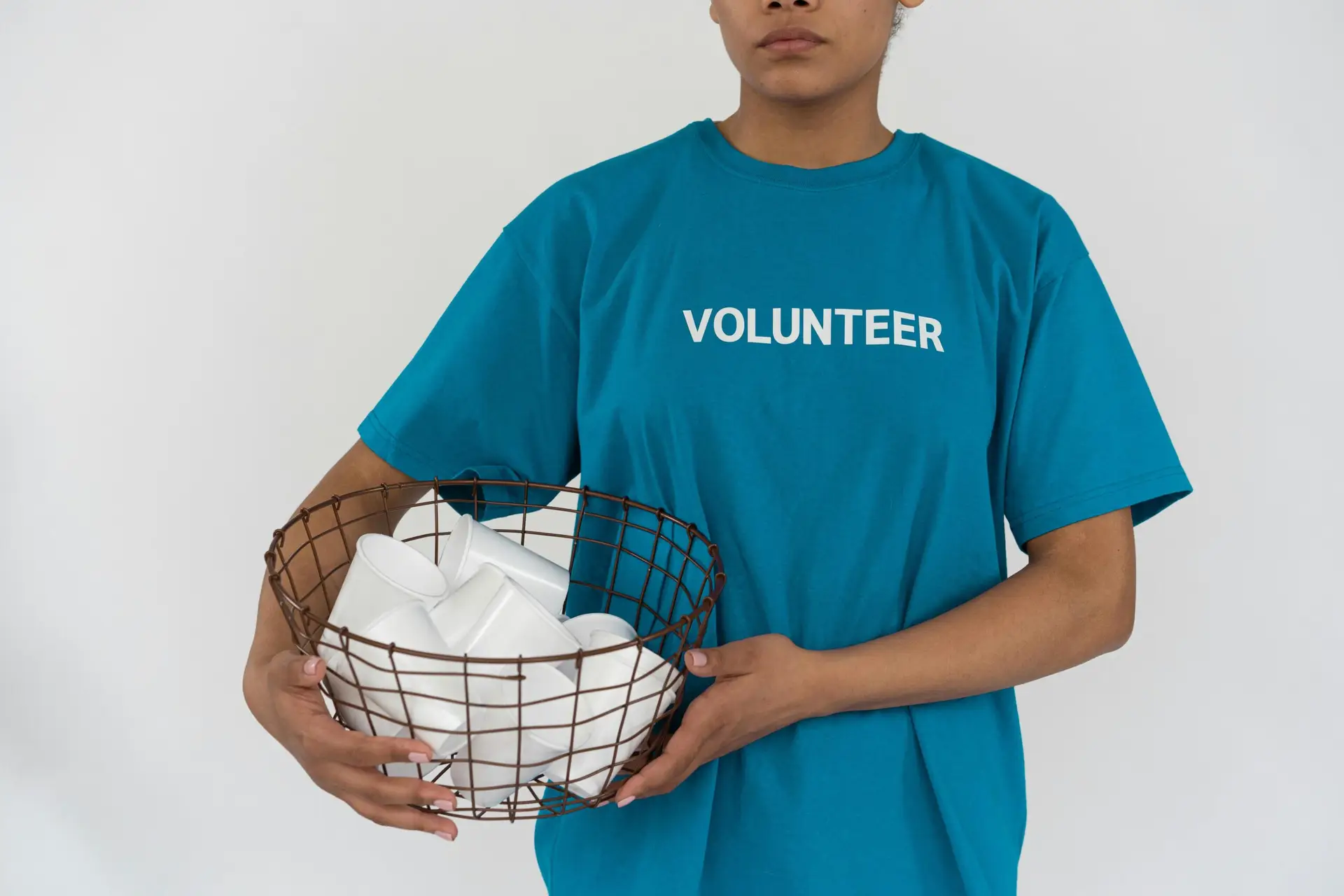 Person in blue shirt holding a metal basket filled with disposable cups, promoting environmental awareness.